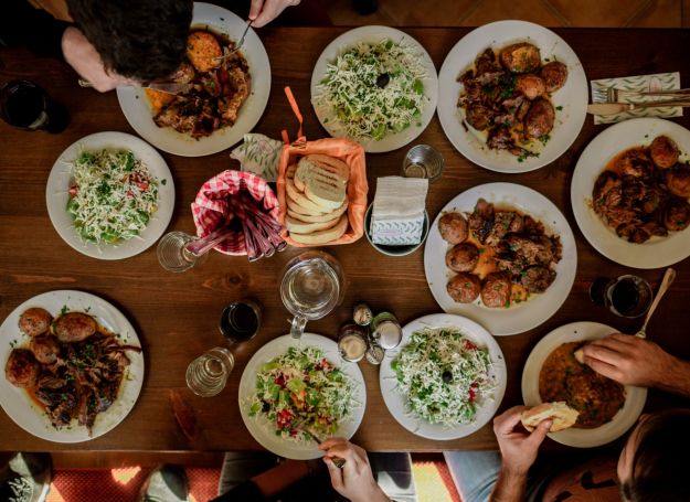 A top view of a dining table at Alta Nova apartments showcases various plates of food, salads, bread, and people seated and eating.